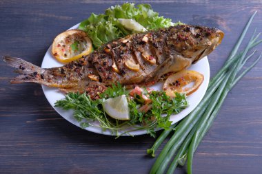 Limon, sarımsak, baharat ve otlar ile fırında pişmiş balık. Carp bir plaka üzerinde yeşillikler ile hizmet