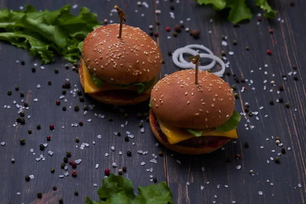 İki Amerikan cheeseburger, peynirli ve sebzeli. Koyu ahşap masada Hamburgerler.