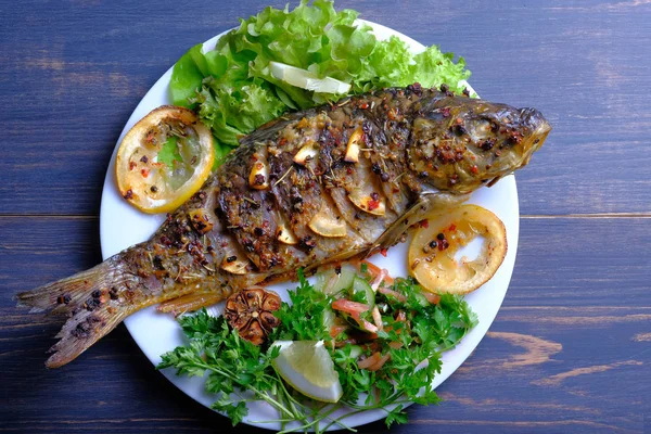 Limon, sarımsak, baharat ve otlar ile fırında pişmiş balık. Carp bir plaka üzerinde yeşillikler ile hizmet