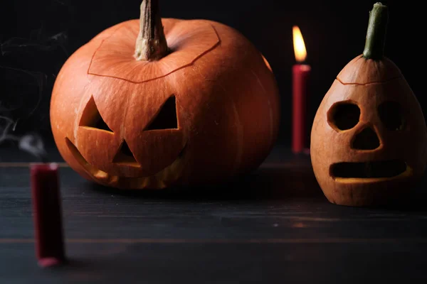 Halloween, two sinister jack-o-lanterns and candles on a dark wooden table.