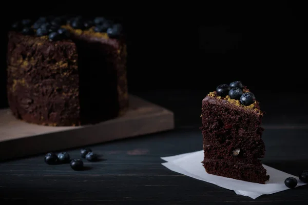 Slice of chocolate cake with cherry and blueberry on a wooden table. Delicious festive dessert. Fresh and beautiful cake.