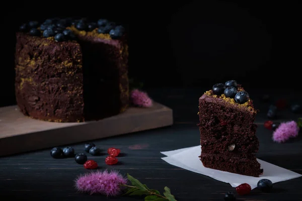 Slice of chocolate cake with cherry and blueberry on a wooden table. Delicious festive dessert. Fresh and beautiful cake.