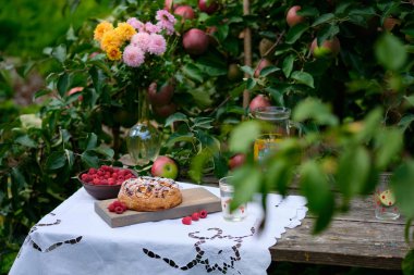 Köydeki bir elma ağacının altındaki eski ahşap bir masada elmalı turta. Parlak güneşli bir gün ve ev yapımı lezzetli bir tatlı..