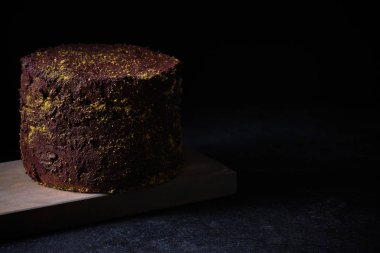 Chocolate cake decorated with ground pistachios on a wooden board.