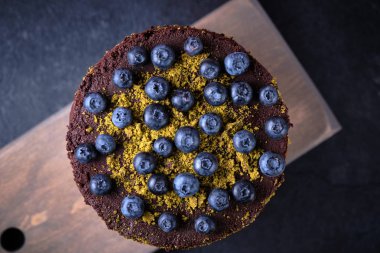 Böğürtlenli çikolatalı pasta ve ahşap bir tahtada yer fıstığı ve böğürtlenlerle süslenmiş kuru kirazlar..