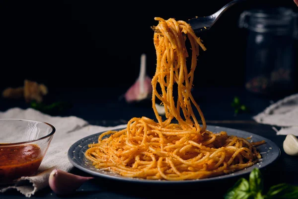 Domates soslu spagetti ve çatallı parmesan peyniri. Koyu ahşap bir tabakta makarna ve malzemeler var. Akşam yemeği için klasik İtalyan yemeği..