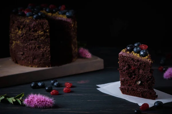 Slice of chocolate cake with cherry and blueberry on a wooden table. Delicious festive dessert. Fresh and beautiful cake.