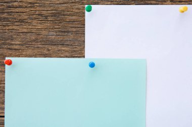 Tahta arka plandaki not defteri kağıdında bir sürü renkli iğne var.