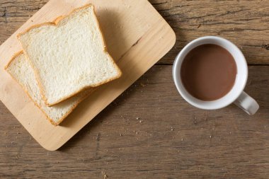 Kahvaltı ekmeğinin ve kahvenin en üst görüntüsü, beyaz bir fincanda, sabah güneşiyle birlikte, ahşap bir masada.