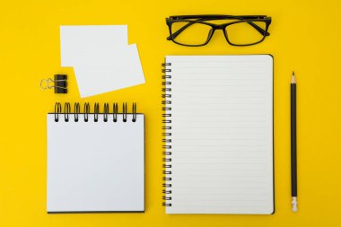 Not defterlerinin, kalemlerin, gözlüklerin, kartvizitlerin, sarı arkaplanda ataçların üst görünümü ve boşluğu kopyala