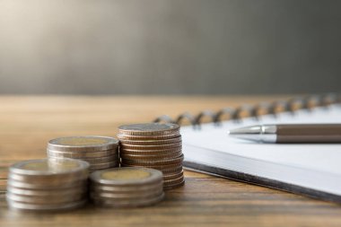 Defterler, madeni paralar, kalemler, ahşap masalar ve güneş ışığı ve kopyalama alanı olan tavan arası duvarları.