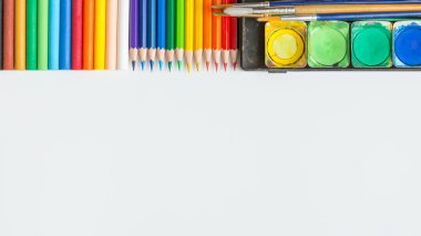 Renkli Suluboya paleti, boya fırçası, renkli kalemler ve beyaz arkaplanda çizim ekipmanlarının üst görünümü