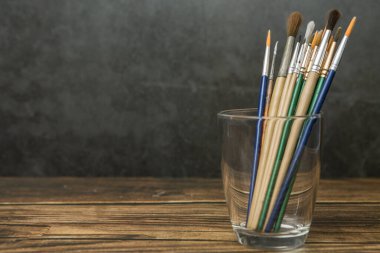 Ahşap ve beton bir duvarın arka planında cam üzerinde birçok sanat fırçası ve kopyalama alanı