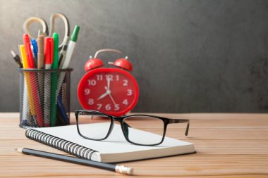 Defterler, kalemlikler, kalemlikler, gözlükler, masalardaki kırmızı alarm saati ve güneş ışığı alan tavan arası duvarları.