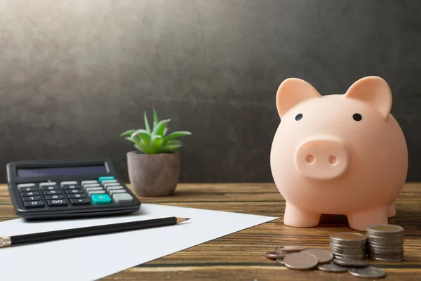 Defterler, domuz kumbarası, madeni paralar, hesap makinesi, kalemler, ahşap masalar ve güneş ışığı alan tavan arası duvarları.