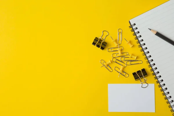 Top view of Notebooks, pens, business card, paper clip on yellow background and copy space