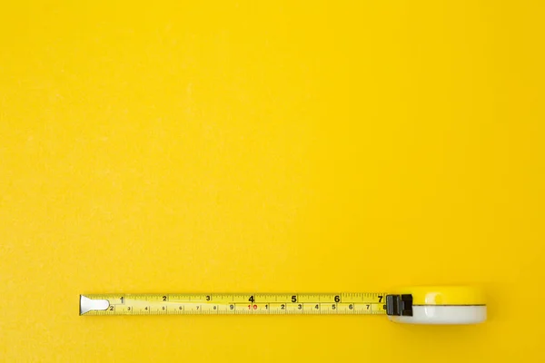 Yellow tape measure on yellow background and copy space