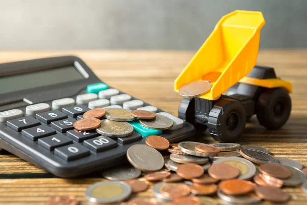 Dump truck, coins stack, calculator on wooden desks and loft walls with sunlight and copy space for money saving concept