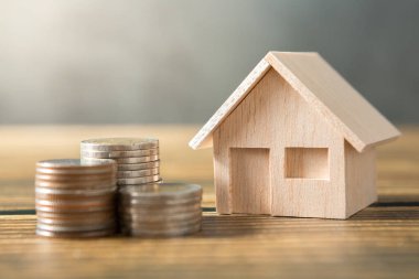 Model ev, madeni paralar ahşap masalara ve tavan arası duvarlarına yığılmış güneş ışığı ve para tasarrufu kavramı için kopyalama alanı