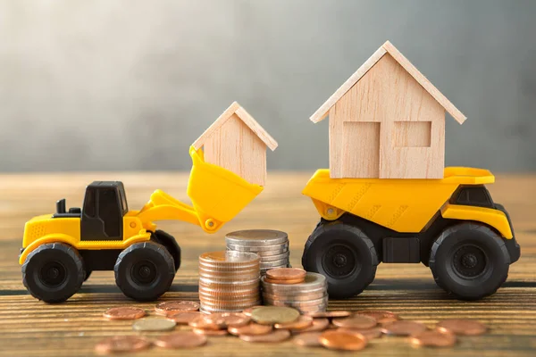 Model house in loader, Dump truck, coins stack on wooden desks and loft walls with sunlight and copy space for money saving concept