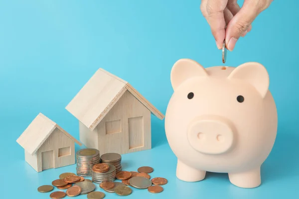 Model house, coins stack, Pig piggy, hand holding a coin bank on blue background for money saving concept