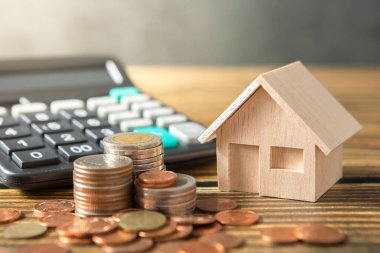 Model ev, madeni para yığını, ahşap masalarda hesap makinesi ve güneş ışığı olan çatı katı duvarları ve para tasarrufu kavramı için kopyalama alanı