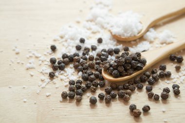 Mutfak masasındaki ahşap kaşıkta siyah biber ve tuz.
