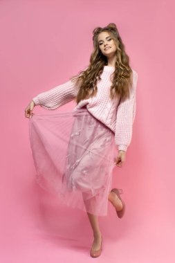 Pembe bir etek neşeli genç kız, örme kazak, odango saç ve kıvırcık uzun saçlı pembe bir arka plan üzerinde topuklu ayakkabılar. pembe toplam görünüm. moda giysiler.