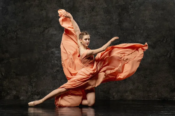 Ballerina. A young ballet dancer dressed in a long peach dress, pointe shoes with ribbons. The girl performs an elegant, graceful dance movement. Beautiful classic ballet. Advertising ballet school.