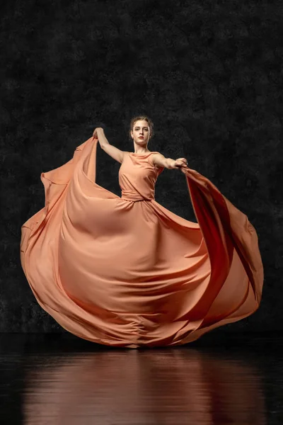 Ba -lerin. Uzun şeftali elbisesi giymiş genç bir dansçı, kurdeleli ayakkabılar. Zarif, zarif bir dans hareketi gerçekleştirir. Güzel klasik bale. Reklam bale stüdyosu. Volumetrik fotoğraflar