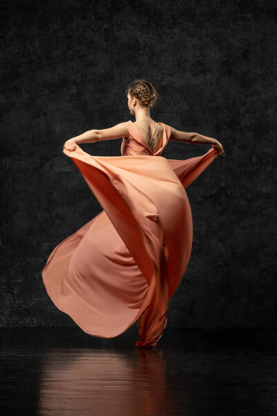Ballerina. A young dancer dressed in a long peach dress, pointe shoes with ribbons. Performs a graceful, graceful dance movement  which is visible from the back. Beautiful classic ballet. 