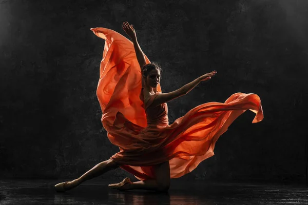 Ballerina. Silhouette photo of a young  ballet dancer dressed in a long peach dress, pointe shoes with ribbons. The girl performs an graceful dance movement. Beautiful classic ballet. Ballet studios.