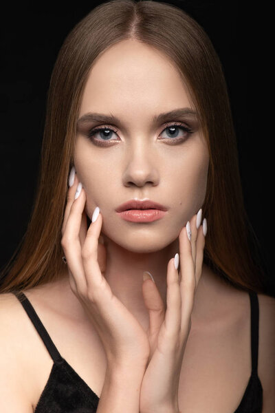 A beautiful young girl charmingly looks with blue eyes, lightly touches her hands to the face with a professional manicure. Advertising nail salon, Salon hairstyles & women barbershop and makeup.