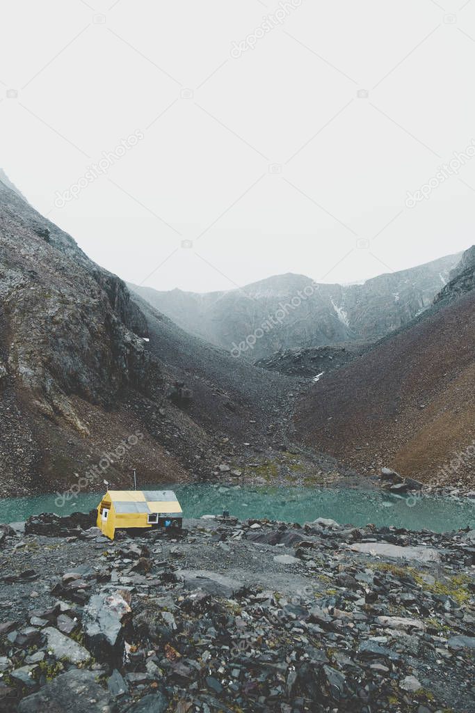 Climbers house on the middle of the ascent to the mountain. Blue lake among the slopes of the mountains. Rocky shore. Showered small stones. Stop in front of a difficult climb. Toned blue photo.