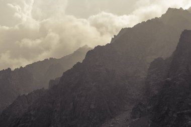 Altay Dağı. Sisli bulutlarda dağ zirveleri. Bulutların arasından güneş ışığı. Altay arazi doğası ile bir turistik gezi yüksek, keskin dağların güzel manzarası. Dağların tonlu fotoğrafı.