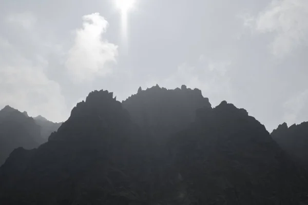 Altay Dağı. Sisli bulutlarda dağ zirveleri. Bulutların arasından güneş ışığı. Altay arazi doğası ile bir turistik gezi yüksek, keskin dağların güzel manzarası.