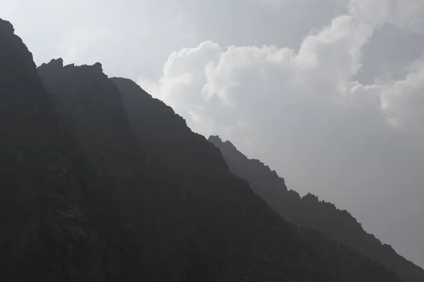 Mountain Altai. Mountain peaks in the misty clouds. Sunlight through the clouds. Beautiful views of high, sharp mountains in a tourist trip through the nature of Altai land.