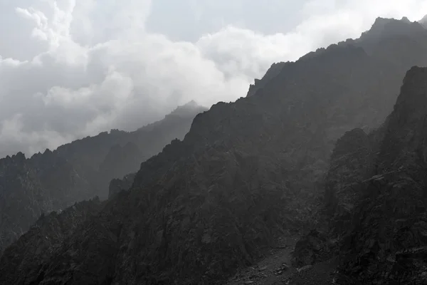 Mountain Altai. Mountain peaks in the misty clouds. Sunlight through the clouds. Beautiful views of high, sharp mountains in a tourist trip through the nature of Altai land.