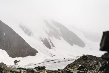 Altay Dağı. Üstünde çok sayıda taş var. Sisli bulutlarda dağ zirveleri. Altay kara doğası ile turistik bir gezi yüksek karla kaplı dağların ve bir buzul güzel manzarası.