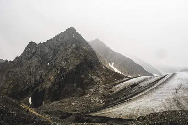 冰川融化附近的高山 岩石斜坡上覆盖着雪 阿尔泰的卷积照片 刺峰被不可穿透的雾所遮蔽 山河的开始 — 图库照片