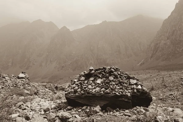 Cairn dağların eteklerindeki taşlar vadisinde. Sisli bulutlarda dağ zirveleri. Tonlu sepya fotoğrafı. Altay doğa turu yüksek dağ güzel manzarası.