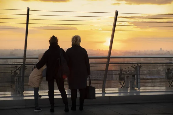 Silhouette of three generations of women watching the sunset from the roof of a skyscraper. Observation deck with a view of the city.