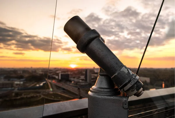 Lookout binoculars. Coin operated binoculars and panoramic view of the city. Sunset. Cracked paint on an old optical device. Red, orange sky and clouds. Sundown.