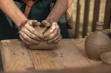 Eski el sanatlarının yeniden inşası. Esnaf çömlek yapmak için kil sıkar. Elinde bir parça kil tutuyordu. Bir atölye çalışması yapıyor. Çömlek sanatları öğretmeni. Masada nasıl heykel yapılacağını gösterir.