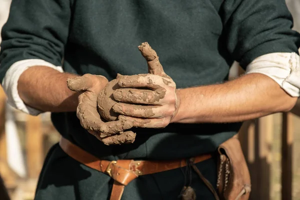 Eski el sanatlarının yeniden inşası. Çömlek yapmak için kil kırışıklıkları. Elinde bir parça kil tutuyordu. Bir atölye çalışması yapıyor. Çömlek sanatları öğretmeni. Nasıl heykel yapılacağını gösteriyor. Eski bir kıyafet giymişti..
