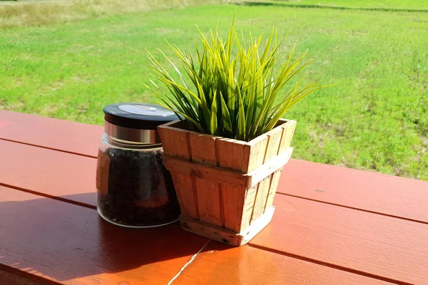 Ahşap bir tencerede plastik ağaç, tarlanın ortasındaki kahve dükkanında kahve şişesi.