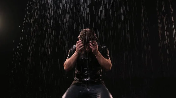 Young guy with long hair stands in the rain at night on the street in a black T-shirt. He is upset and falls to the ground and hits her with his hands. The concept of friend leaving life or big loss.