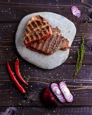 Kırmızı biber ve soğan ile ahşap arka plan üzerinde gri taş üzerinde Sığır eti biftek