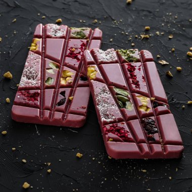 Hindistan cevizi cips, fıstık, antep fıstığı, kurutulmuş ahududu ve koyu arka plan üzerinde erik ile pembe ahududu çikolata iki sopa yakın çekim