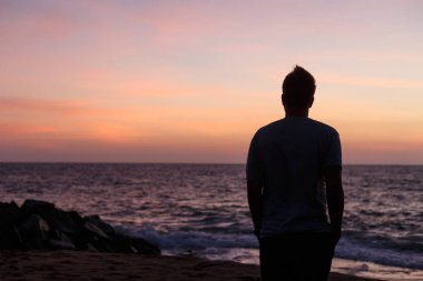 Gün batımında okyanusa karşı bir adamın silueti